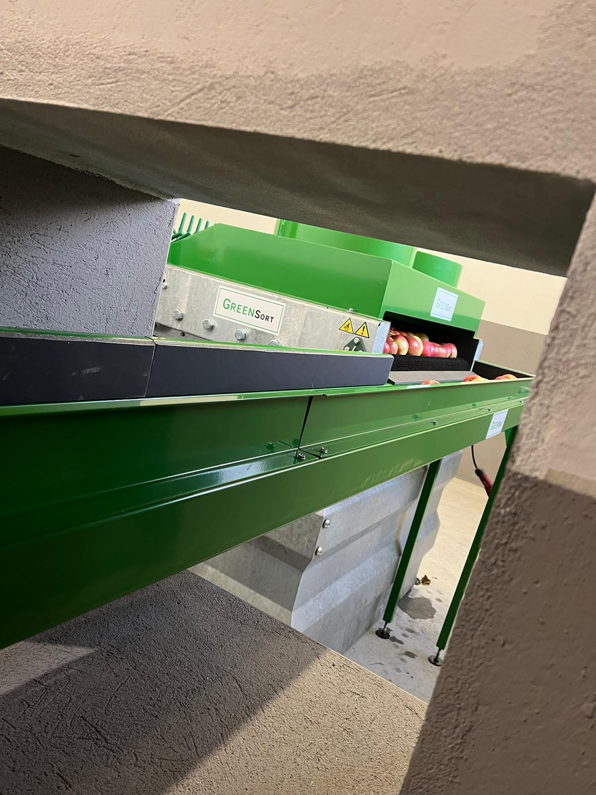 Moduł transportu jabłek w kompaktowej linii sortującej Green Sort przeprowadzony przez otwór w ścianie